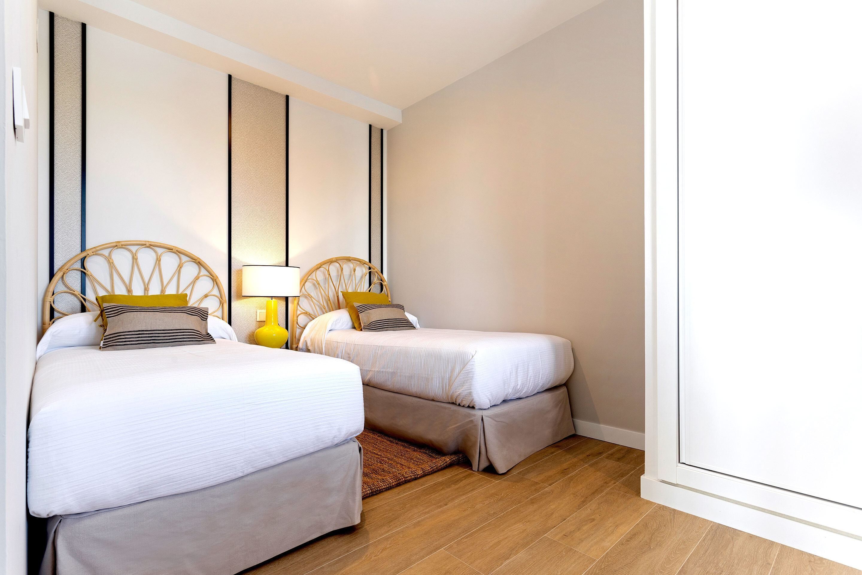 Une chambre d’hôtel avec deux lits simples, une table de chevet avec une lampe et un plancher en bois.