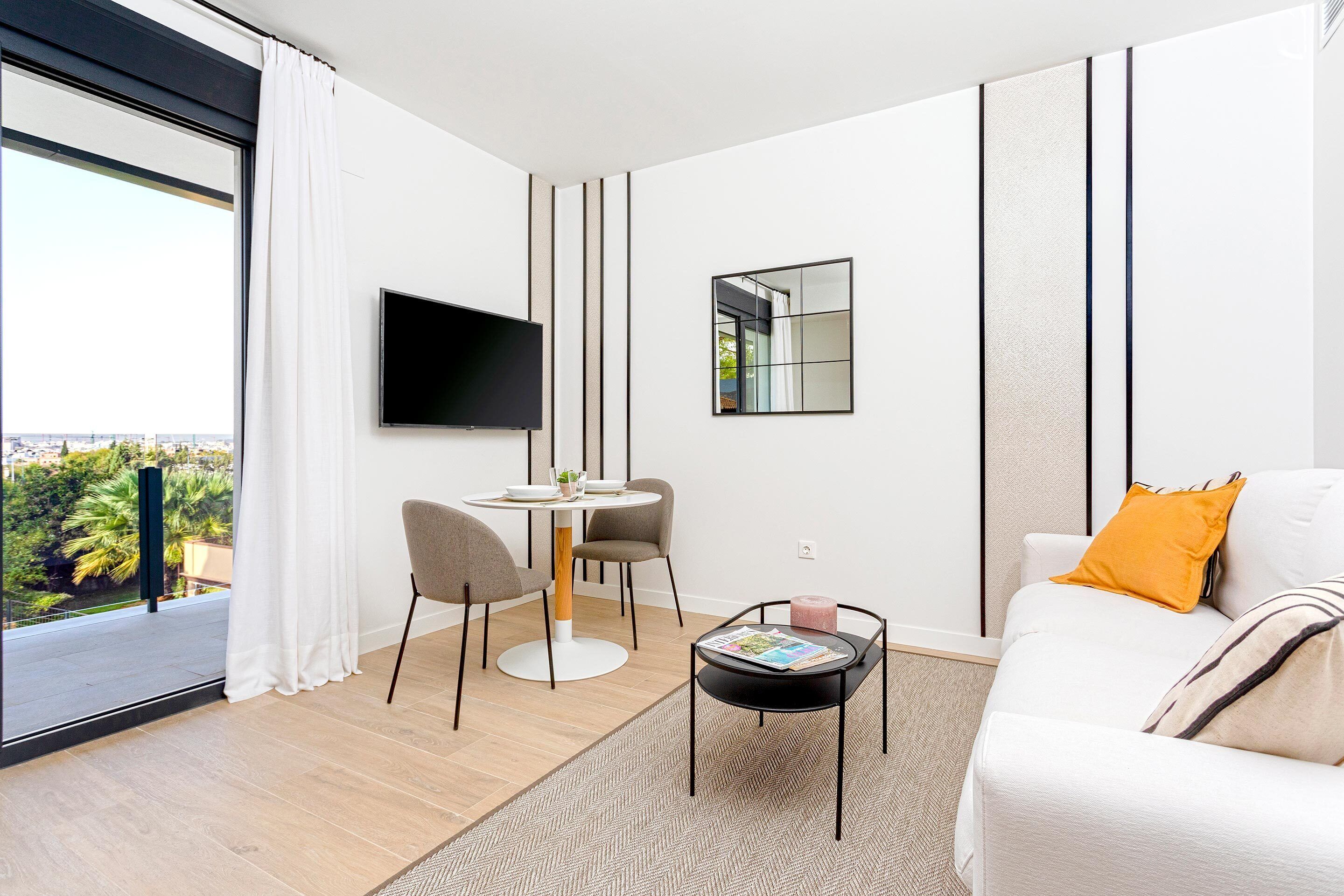 Una sala de estar moderna con sofá, mesa de centro, televisor y comedor con sillas y mesa.