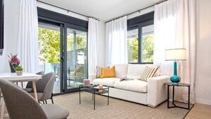 A modern living room with a white sofa, a glass door leading outside, a small table, and a lamp.