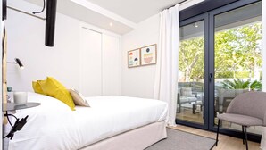 A bedroom with a bed, a chair, a table with a cup, and a window with curtains.