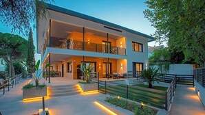 A modern two-story house with a balcony, outdoor seating area, and a well-lit pathway.