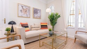 A living room with a beige sofa, a glass coffee table, a potted plant, and abstract paintings on the wall. - Genteel Home San Isidoro (Seville)