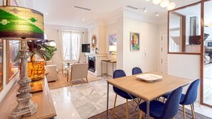 A modern living room with a fireplace, a dining area with blue chairs, and a kitchen visible through an open door. - Genteel Home San Isidoro (Seville)