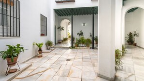 A spacious courtyard with tiled flooring, potted plants, and a central archway leading to another area. - Genteel Home San Isidoro (Seville)