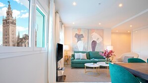 Ein modernes Wohnzimmer mit großem Fenster, einem grünen Sofa, einem Esstisch und einem Fernseher.