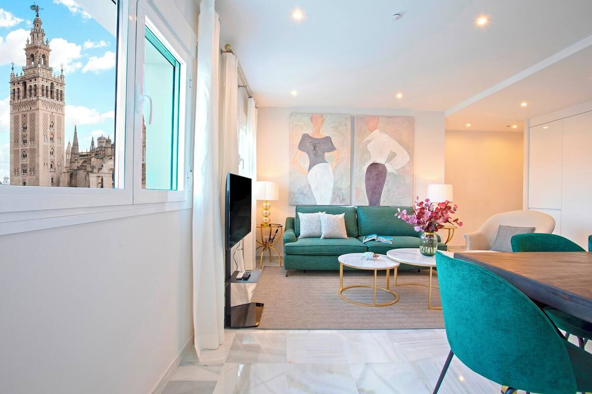 Een moderne woonkamer met een groot raam, een groene bank, een eettafel en een televisie.