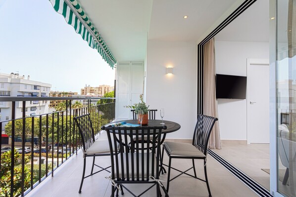 A balcony with a round table and chairs, a potted plant, and a TV on the wall.