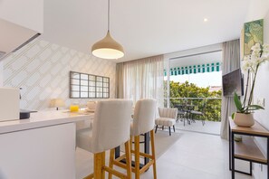 A modern kitchen with a dining area, a balcony with a view, and a TV on the wall.