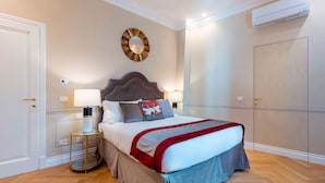 A neatly arranged bedroom with a bed, bedside lamps, a round mirror, and an air conditioning unit. - Genteel Home Via della Spada (Florence)