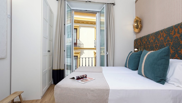 Una habitación de hotel con cama, un banco y vistas a un balcón.
