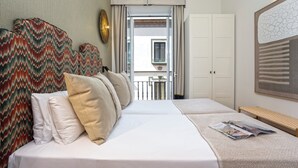 Habitación de hotel con cama, banco, puerta y vista al balcón exterior.