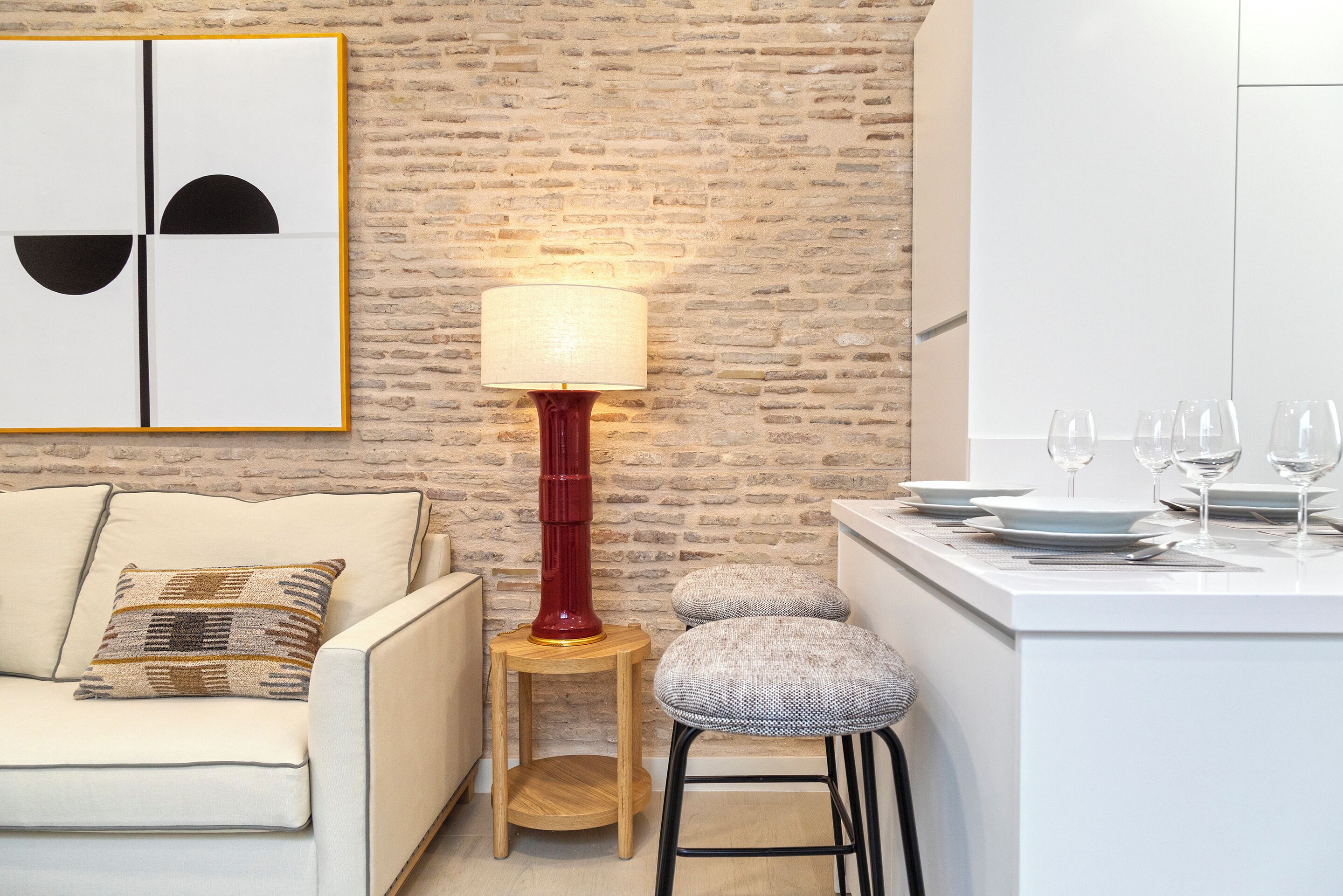 A modern kitchen with a brick wall, a white countertop, and a red floor lamp.