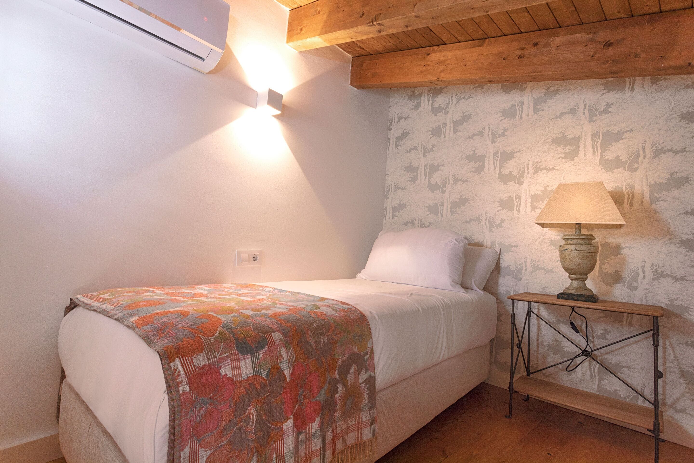 A bedroom with a bed, a nightstand, a lamp, and a wall with a patterned wallpaper.
