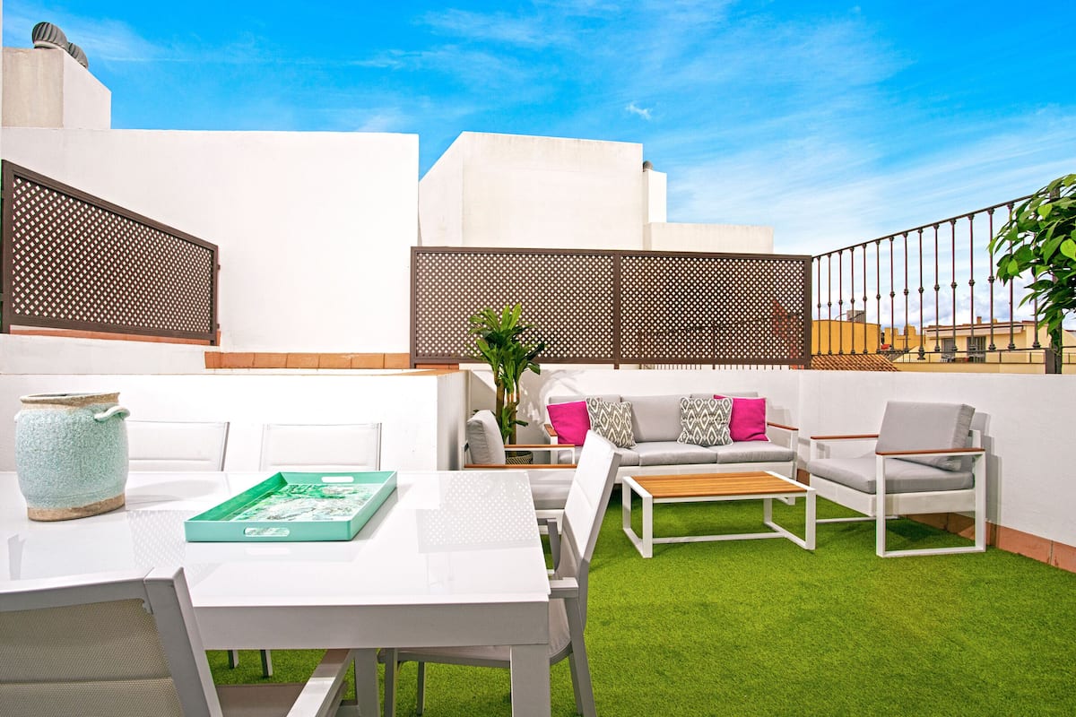 A modern outdoor living space with a white table, chairs, and a sofa.