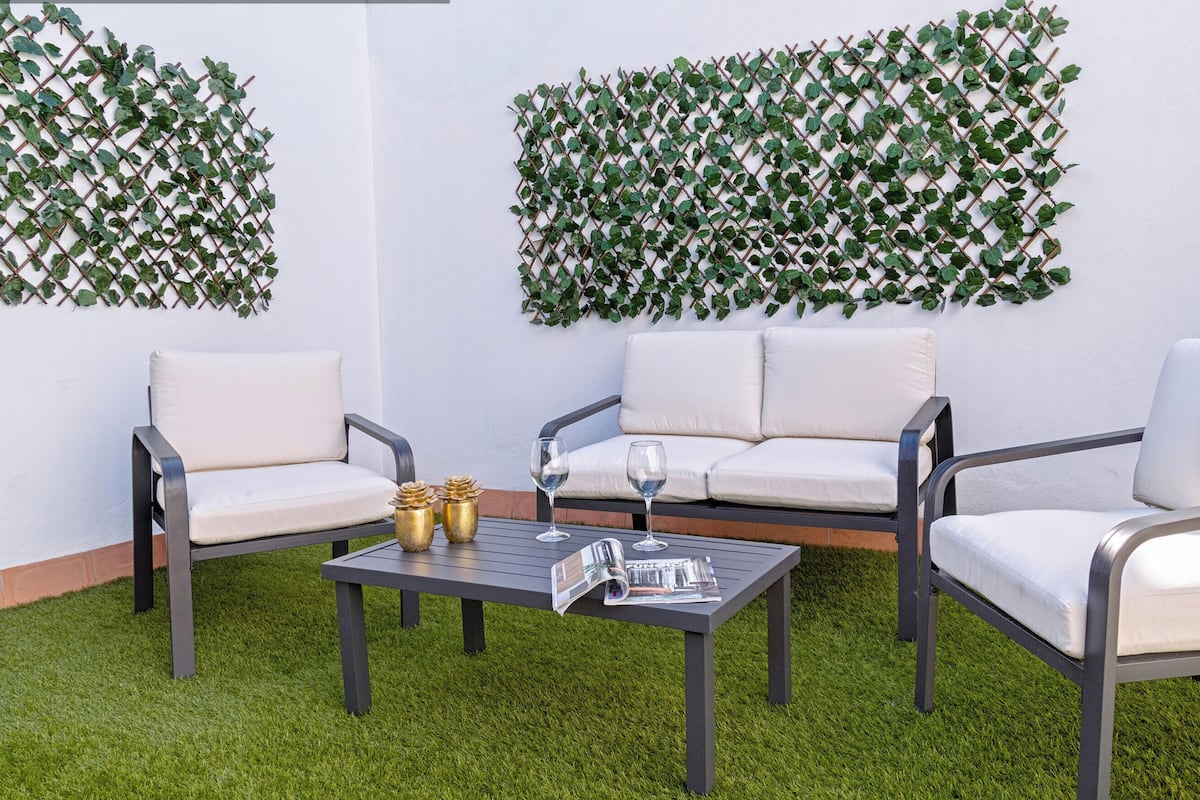 A private terrace with a white wall, two white cushioned chairs, a small table with a magazine, and two wine glasses.