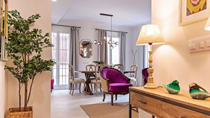 A modern dining area with a chandelier, a purple chair, and a table with chairs. - Genteel Home Feria (Seville)