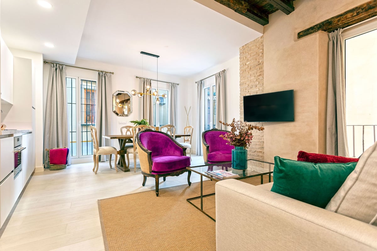 A modern living room with a sofa, two armchairs, a coffee table, and a TV mounted on the wall.