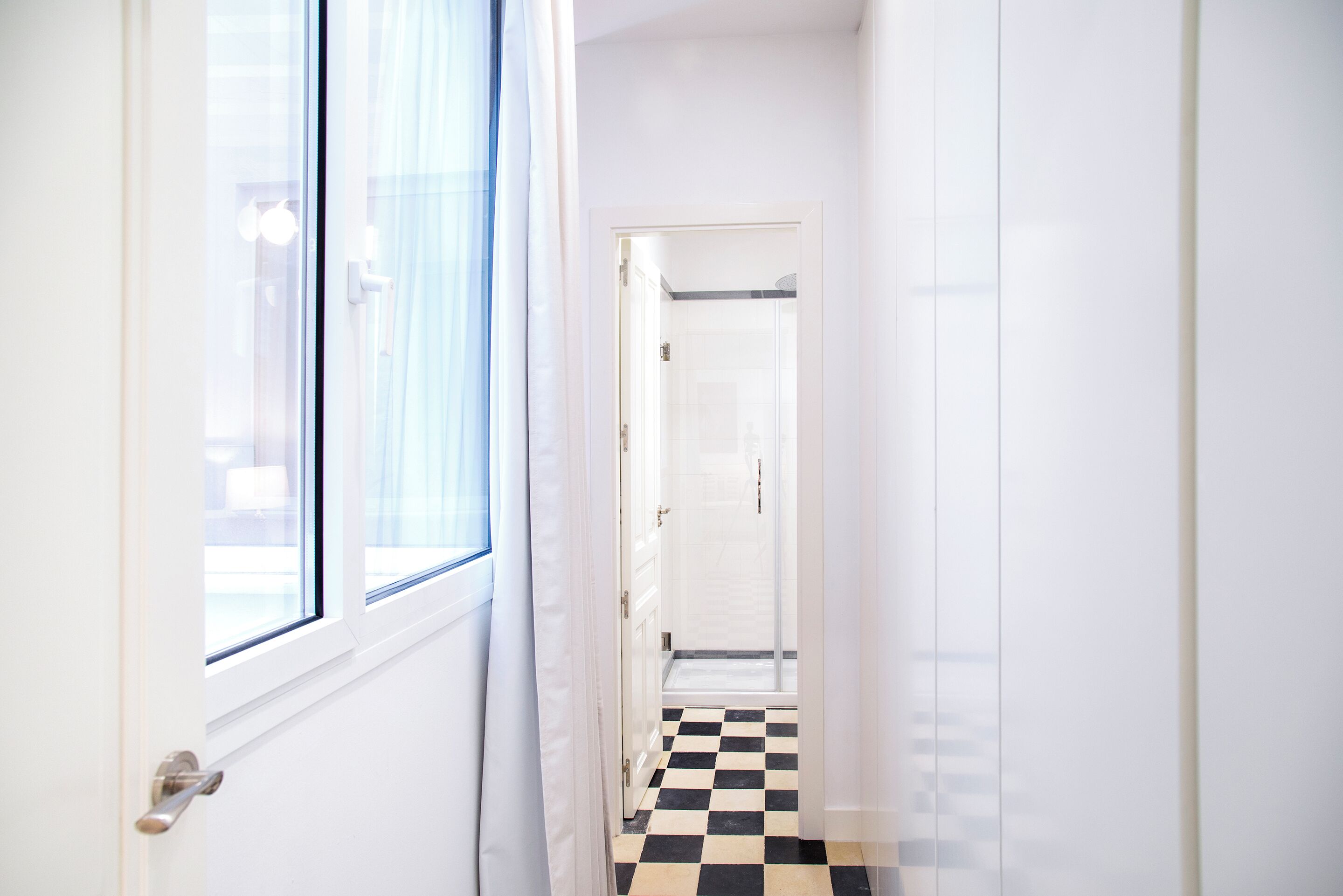 A narrow hallway with a checkered floor, white walls, and a door leading to a room.