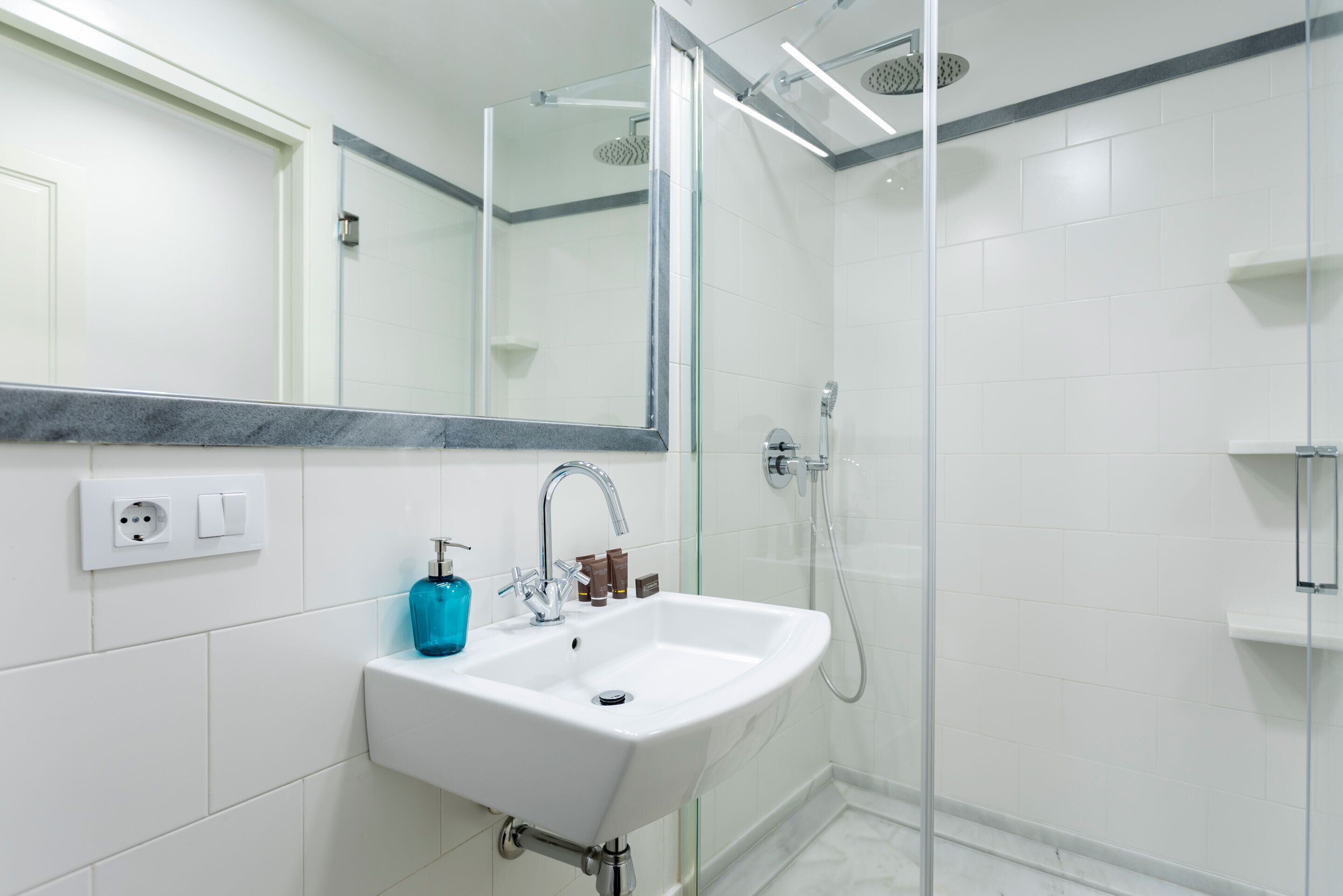 A modern bathroom with a white sink, a glass shower enclosure, and a large mirror.