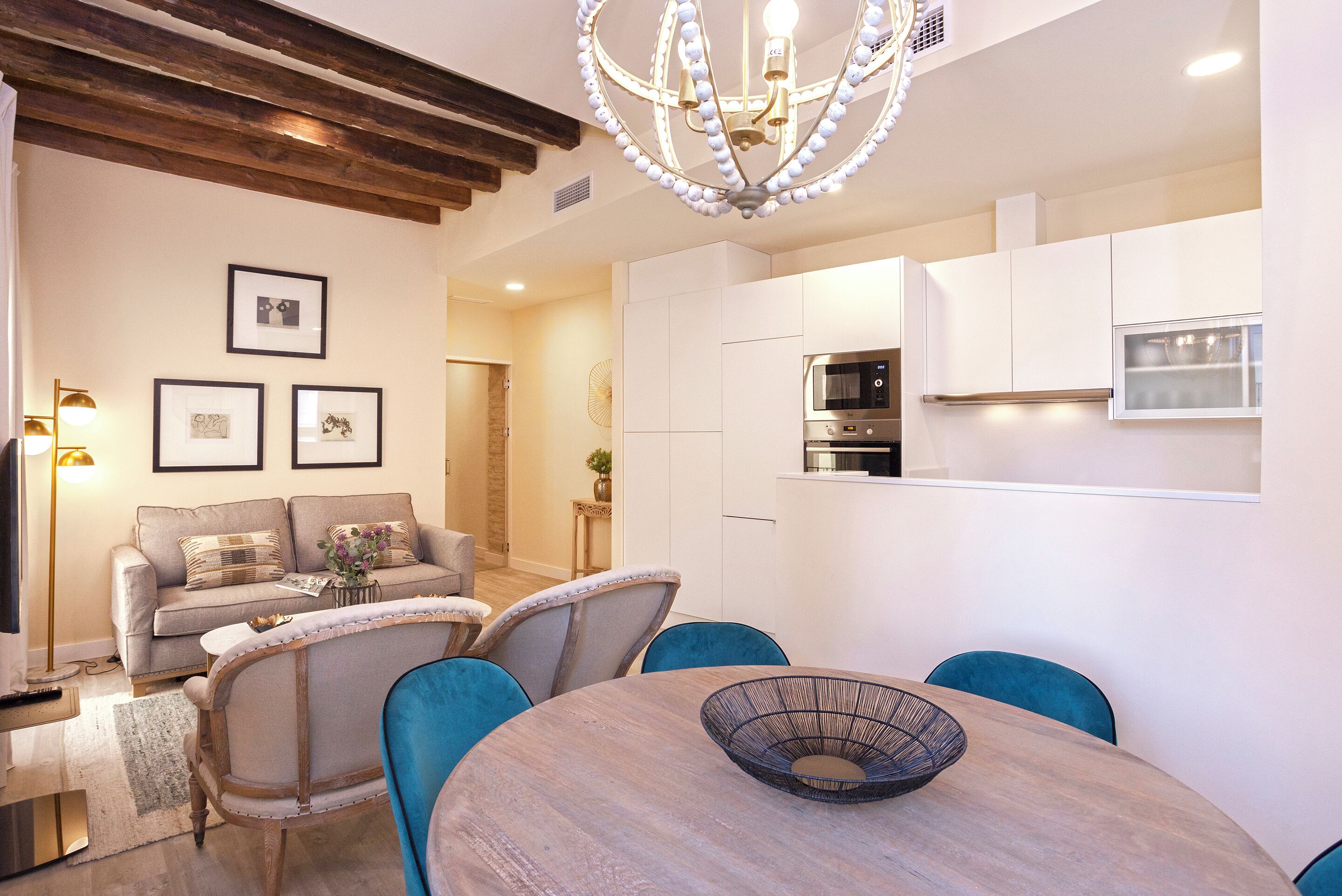 A modern kitchen with white cabinets and a built-in oven. There is a dining area with a round table and blue chairs.