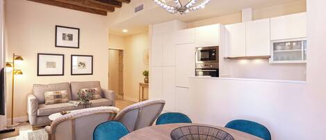 A modern kitchen with white cabinets and a built-in oven. There is a dining area with a round table and blue chairs.