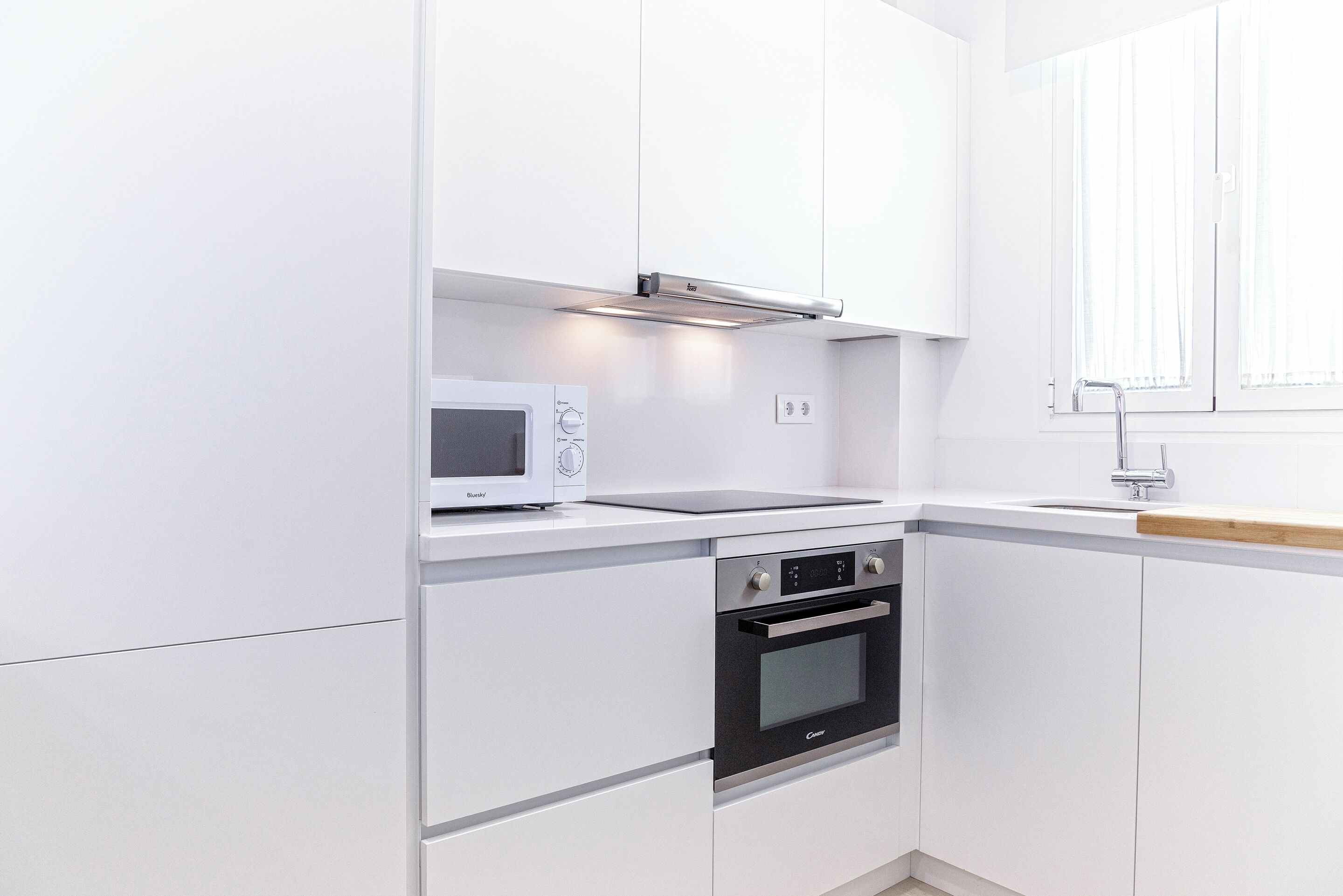 A modern kitchen with white cabinetry, a built-in microwave, a stove, and a sink.