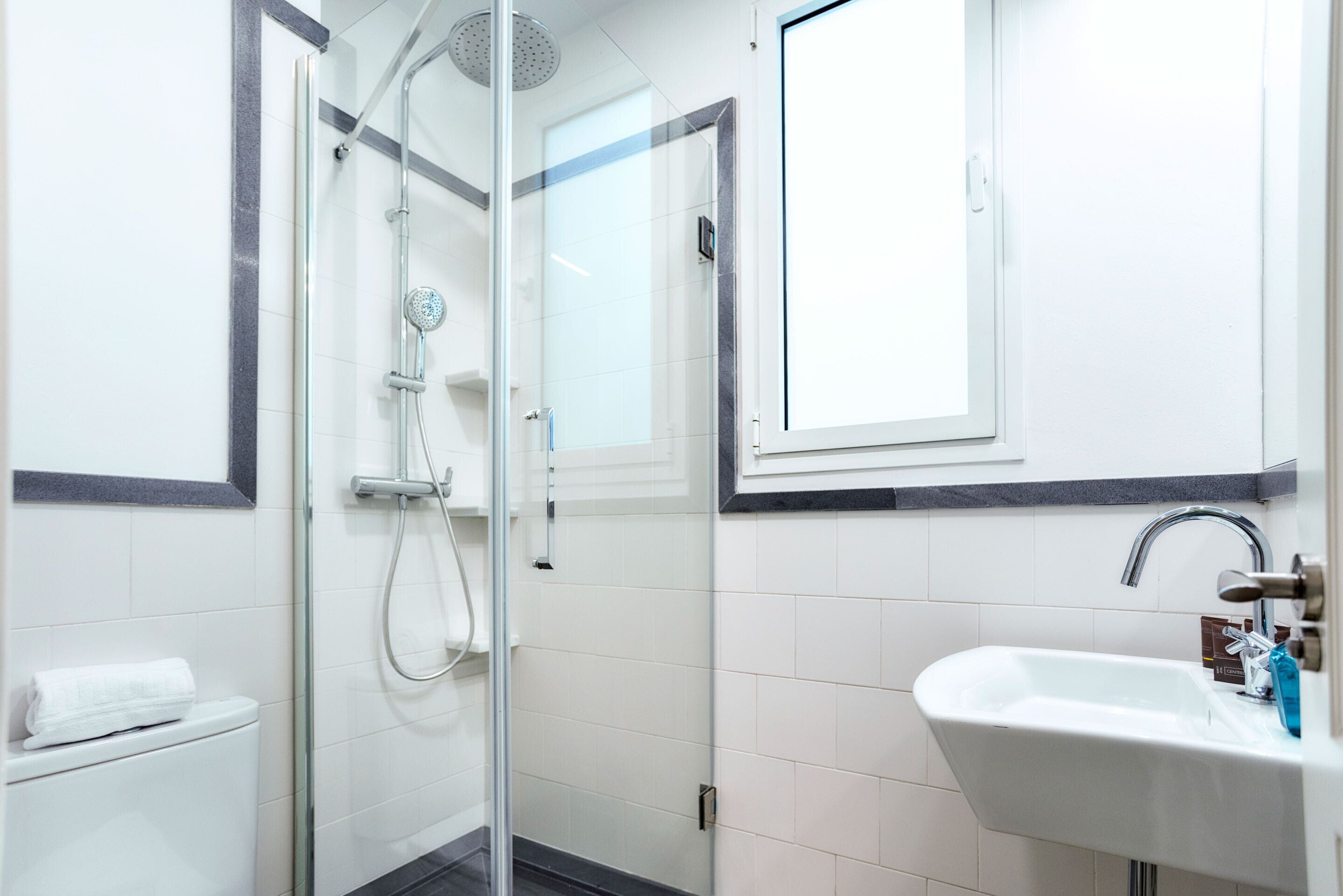 Un bany modern amb dutxa envidrada, un lavabo blanc i un escurapulides.