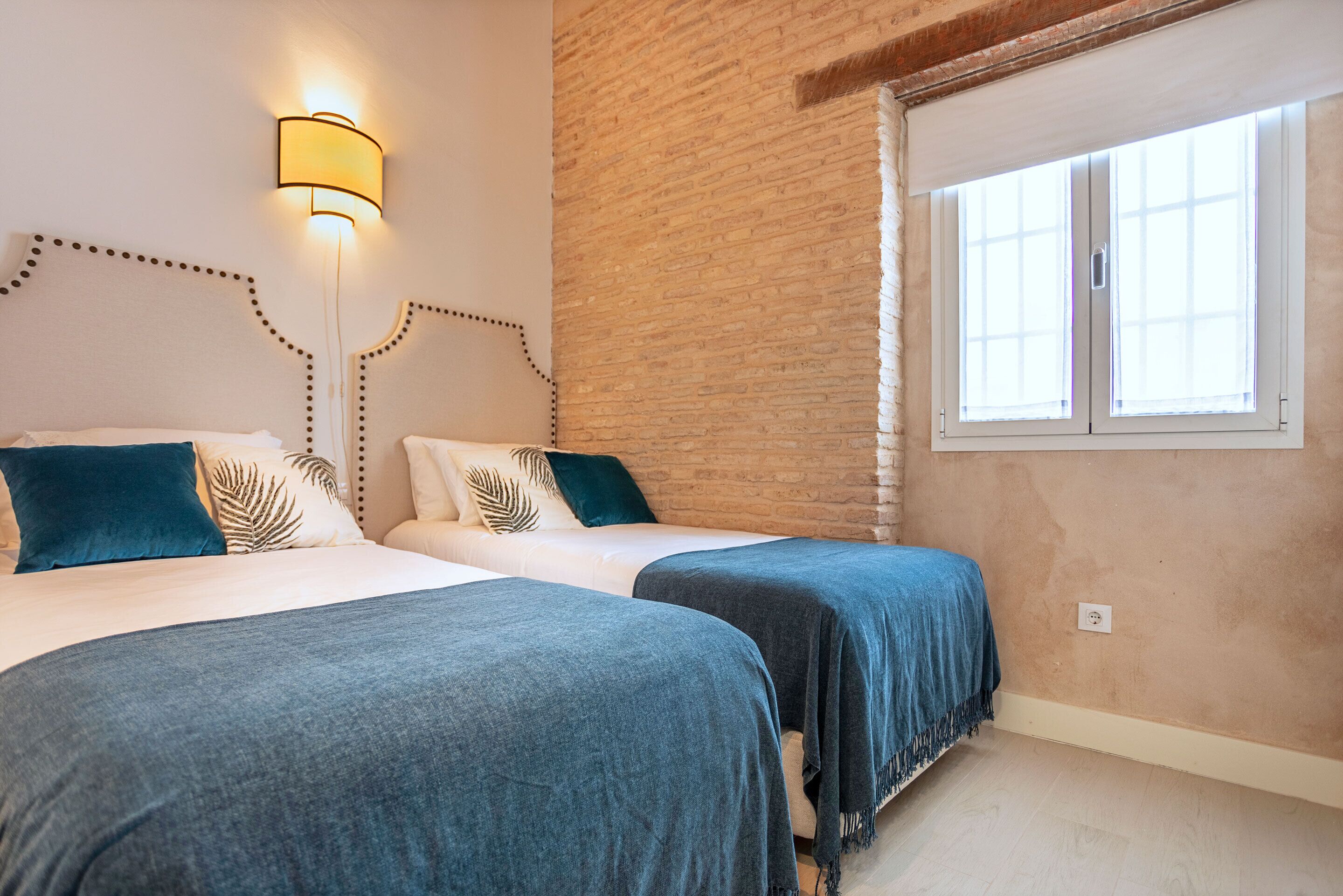 Une chambre avec deux lits, un mur en briques et une fenêtre.