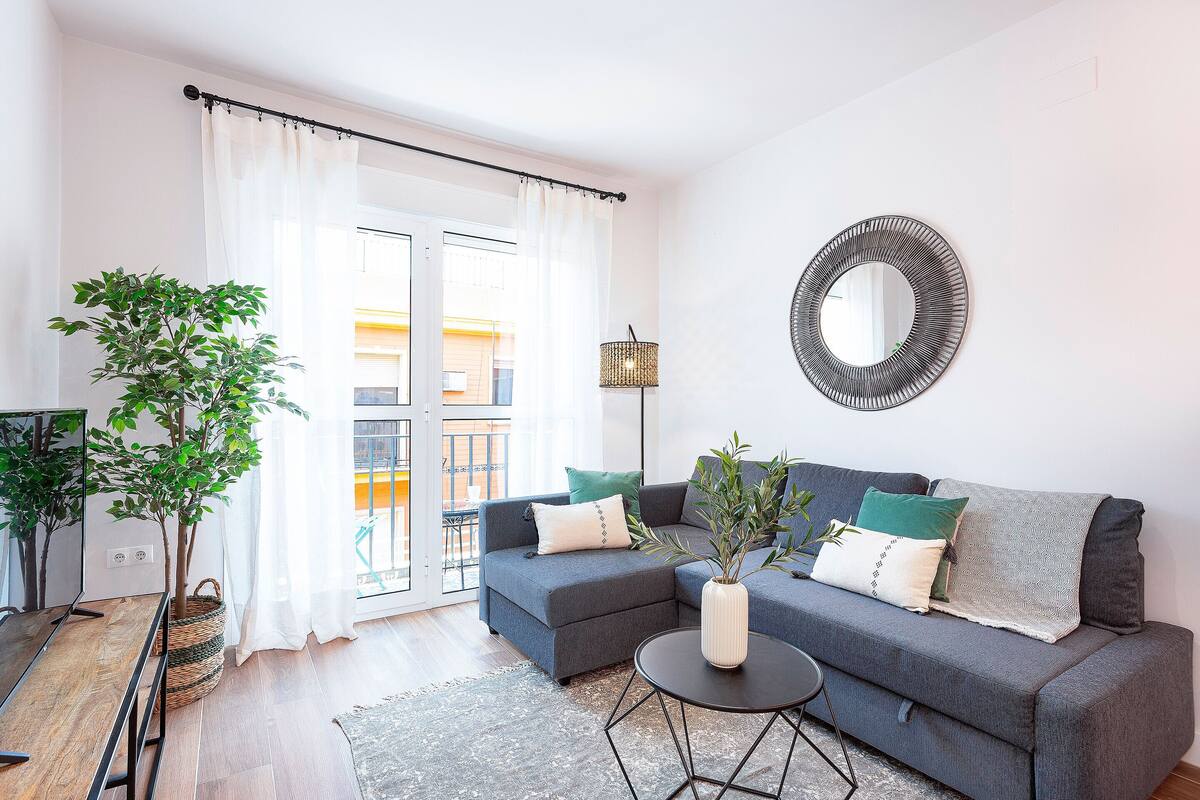 Un salon moderne avec un canapé gris, un miroir rond et une plante en pot.