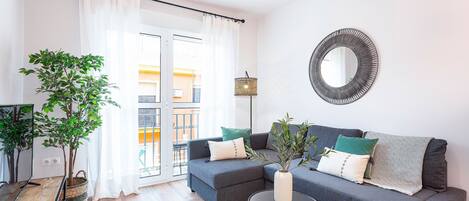 A modern living room with a grey sofa, a round mirror, and a potted plant.
