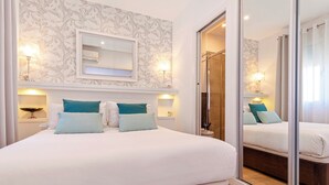 Une chambre avec un grand lit, deux tables de chevet avec des lampes, un miroir au-dessus du lit et une porte-fenêtre coulissante donnant sur une salle de bain.