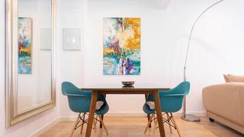 Una habitación moderna con una mesa de comedor de madera, dos sillas color turquesa y un sofá color beige. Hay cuadros abstractos en la pared y una lámpara de pie.