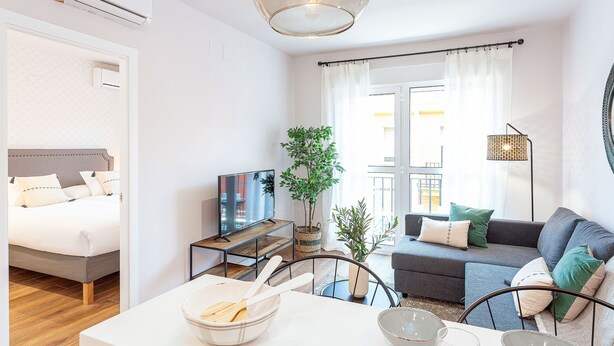 Un salon moderne avec un canapé, une table à manger avec des bols, un téléviseur et une plante.