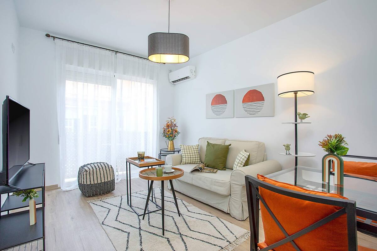 Un salon moderne avec un canapé, une table basse et des fauteuils, un téléviseur et des œuvres d’art accrochées au mur.