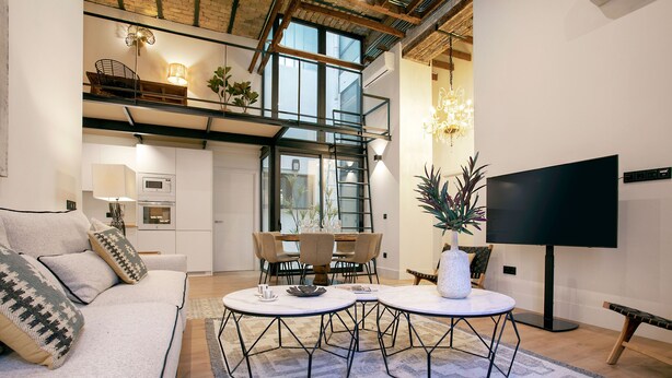 A modern living room with a sofa, two round tables, a TV, and a dining area with chairs and a table. - Genteel Home Almansa (Seville)