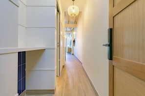 Un couloir moderne avec un plancher en bois, des murs blancs et un luminaire suspendu.