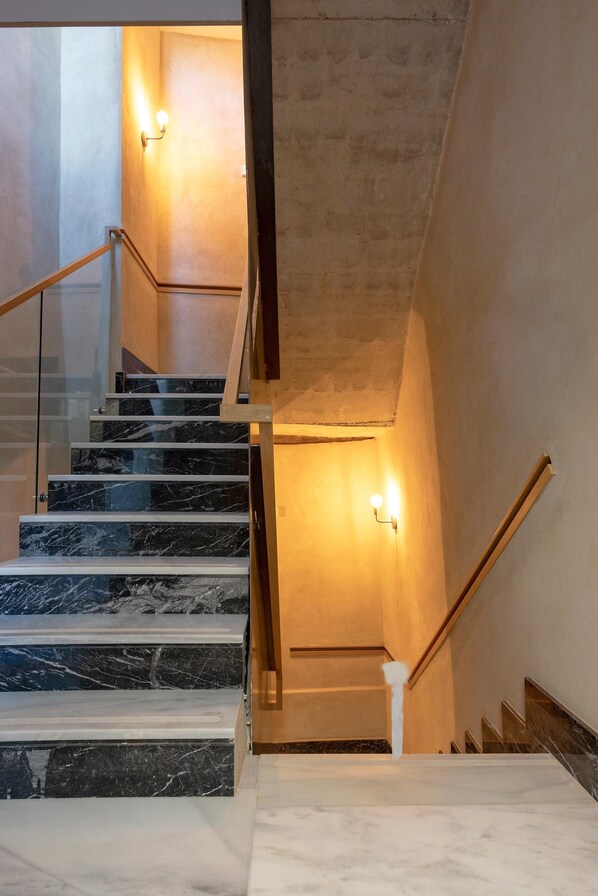 Un escalier moderne avec des marches en marbre et des rampes en bois, éclairé par des appliques murales.