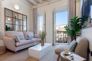 A modern living room with a sofa, coffee table, and a balcony with a view of buildings. - Genteel Home San Francisco (Seville)