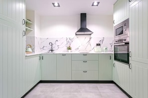 A kitchen with light green cabinets, a black range hood, a double oven, and marble backsplash. - Genteel Home San José (Granada)