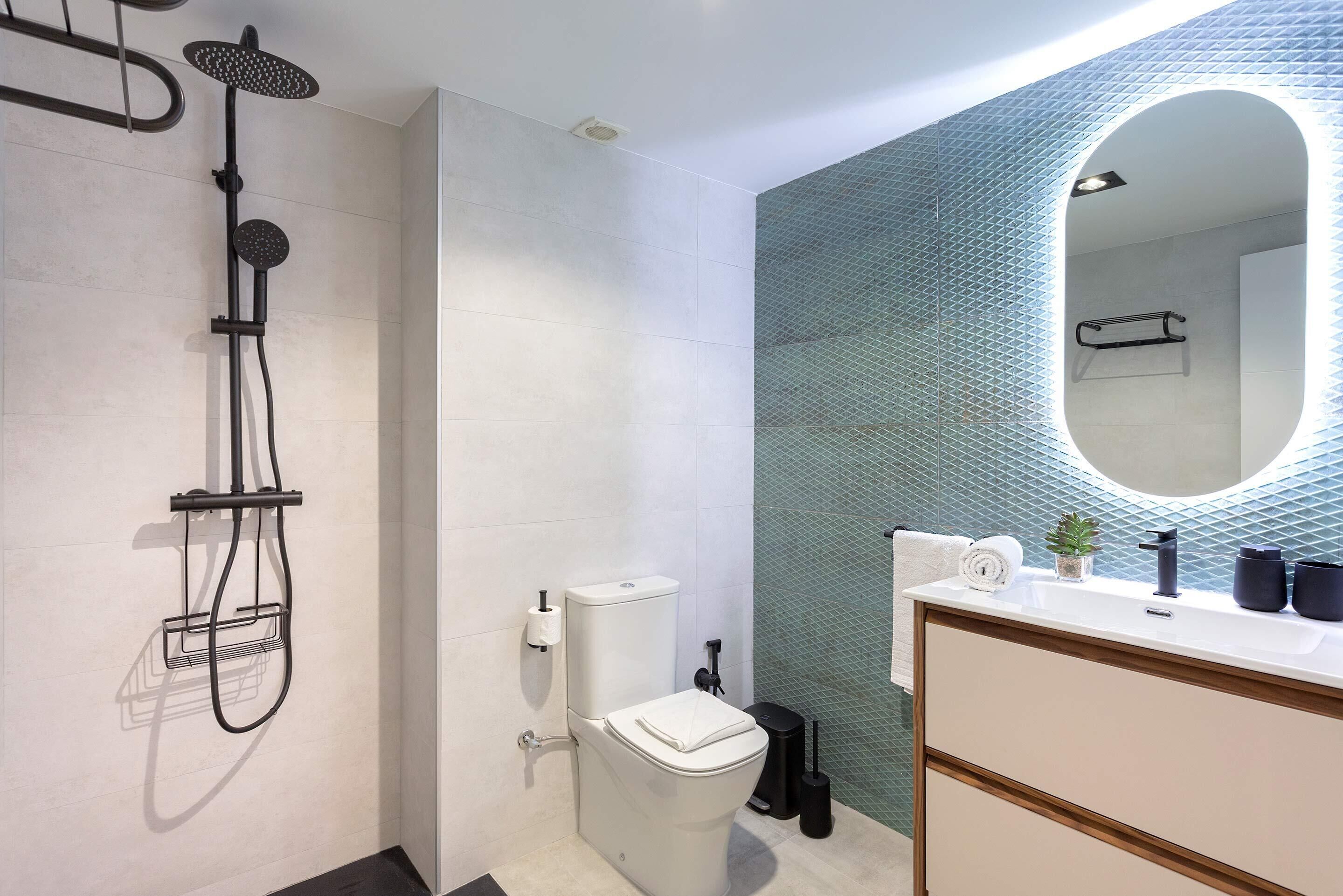 Un baño moderno con ducha, inodoro, lavamanos y espejo con un elegante revestimiento geométrico.