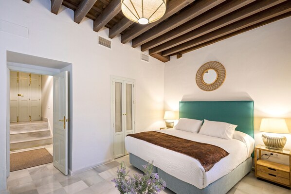 A bedroom with a bed, bedside tables, a mirror, and a staircase leading to a hallway. - Genteel Home Palacio Abades Terrace (Seville)