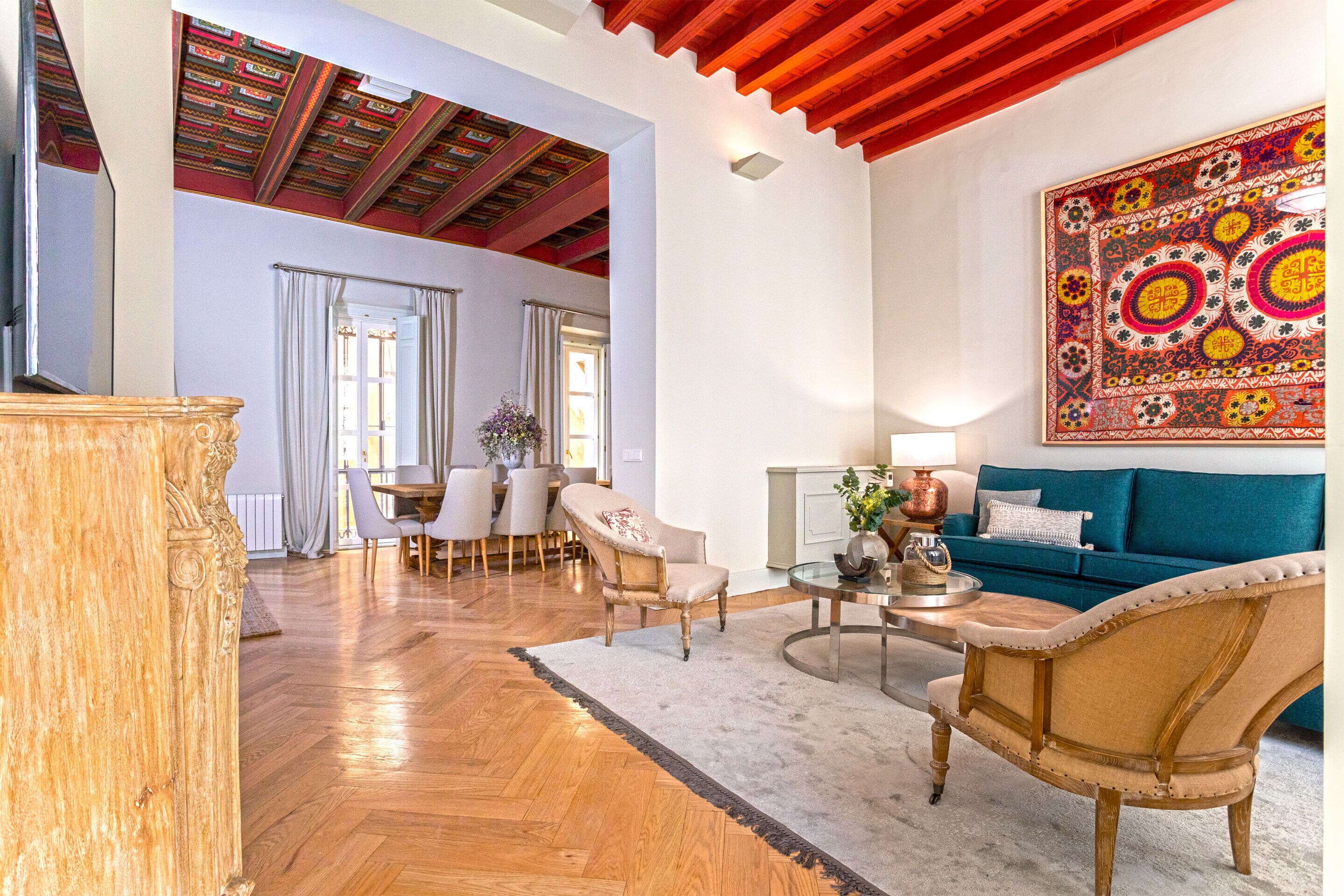 A spacious living room with a wooden floor, a blue sofa, a wooden coffee table, and a dining area with a table and chairs.