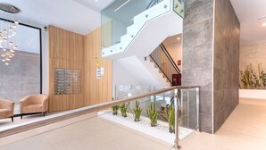 Un vestíbulo moderno con escalera de cristal, zona de estar y mostrador de recepción.