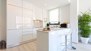 Una cocina moderna con armarios blancos, una isla central con taburetes altos, un microondas y una planta en maceta.