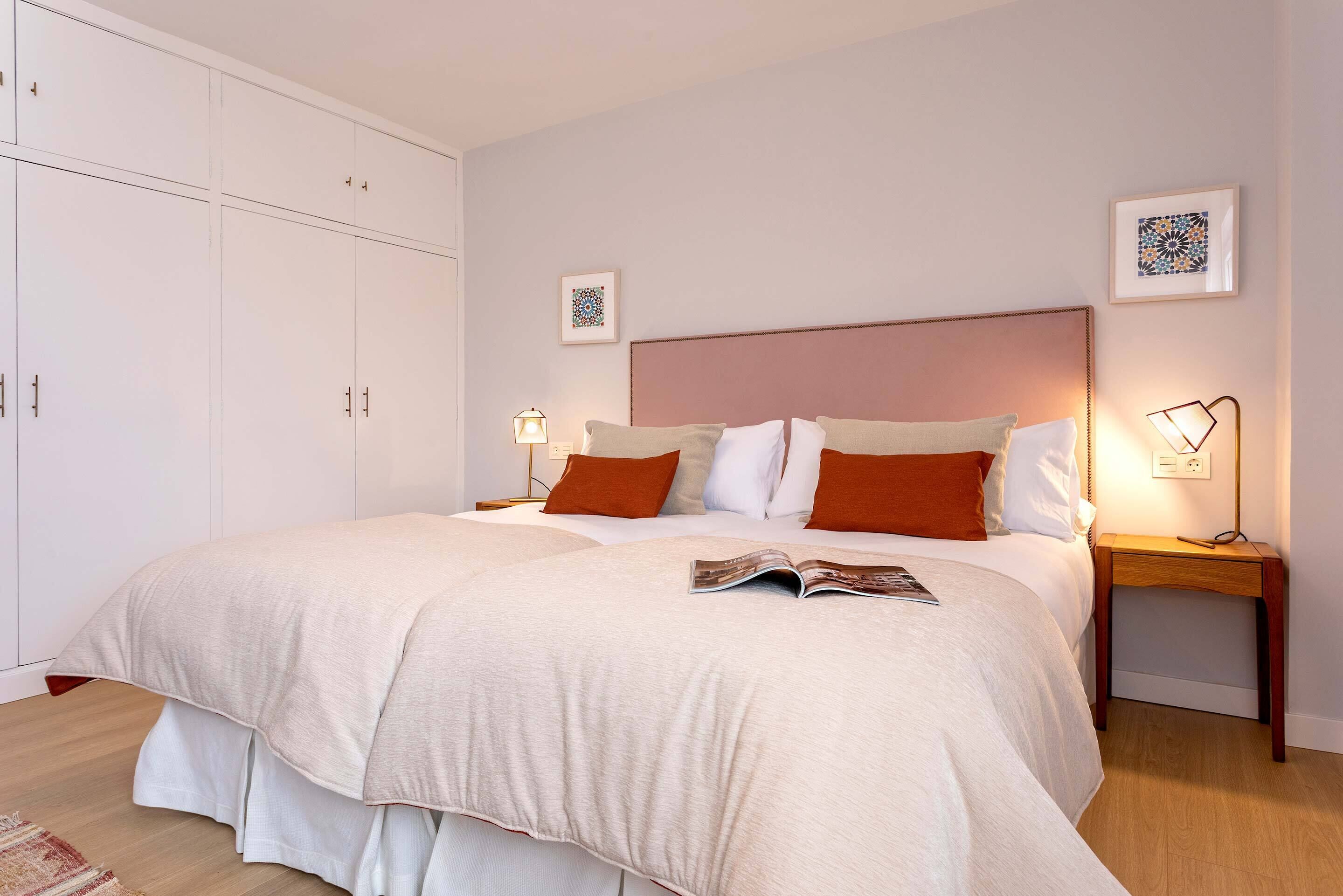 A neatly arranged bedroom with a large bed, two bedside tables with lamps, a wardrobe, and framed artwork on the walls.
