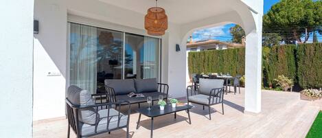 Un espacio al aire libre cubierto con una mesa y sillas, una lámpara colgante y vistas a un edificio y árboles al fondo.