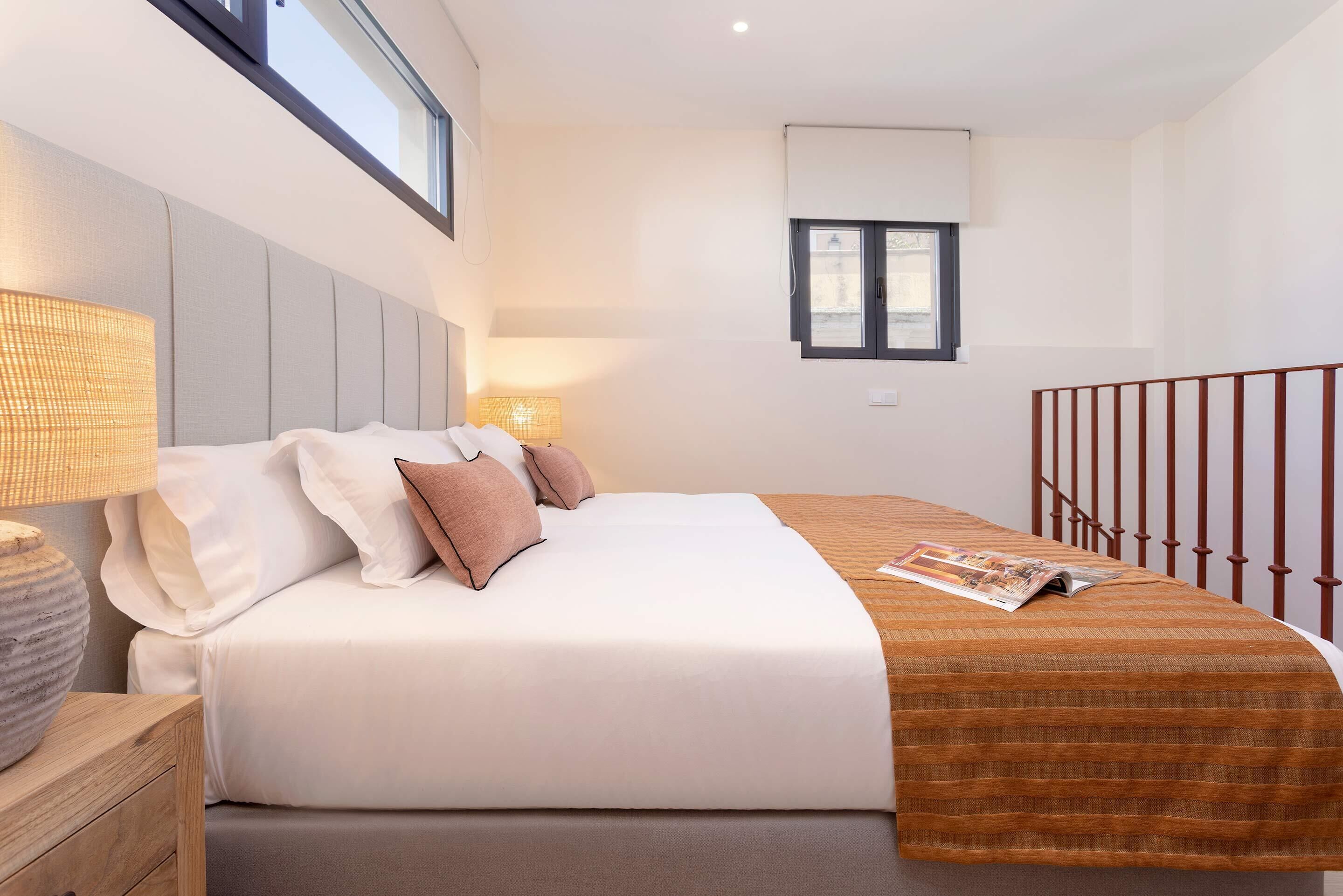 A modern bedroom with a large bed, bedside lamps, a window, and a wooden nightstand.