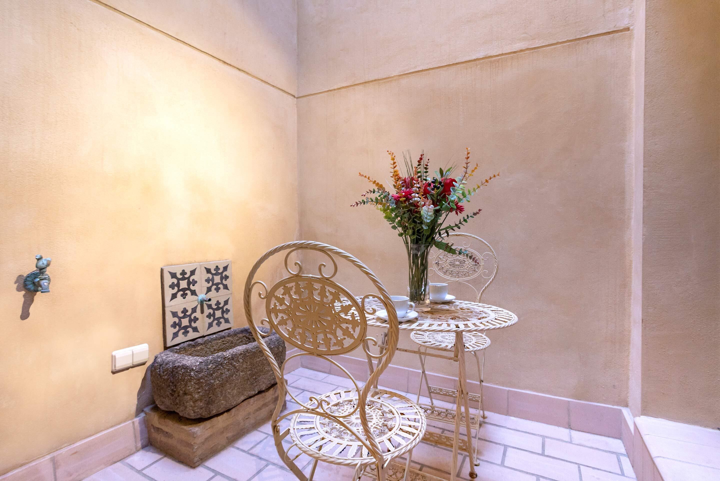 Un coin de pièce avec une chaise en métal blanche, une petite table sur laquelle est posé un vase de fleurs et un élément décoratif mural.