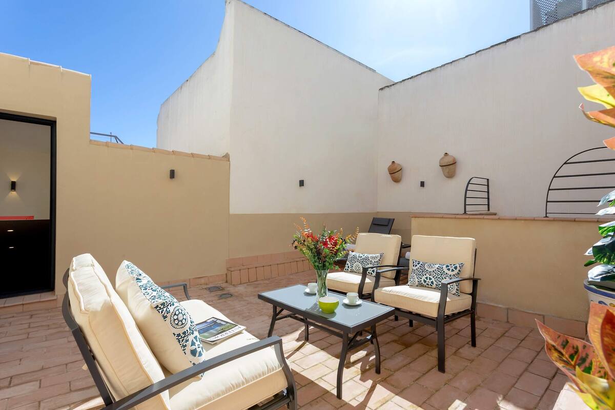 An outdoor patio with a sofa, chairs, a table, and a vase of flowers.