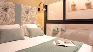 A neatly made bed with a green blanket and pillows, a book on the bed, a wall with a decorative pattern, and a window with two vases. - Genteel Home Rodrigo Caro (Seville)